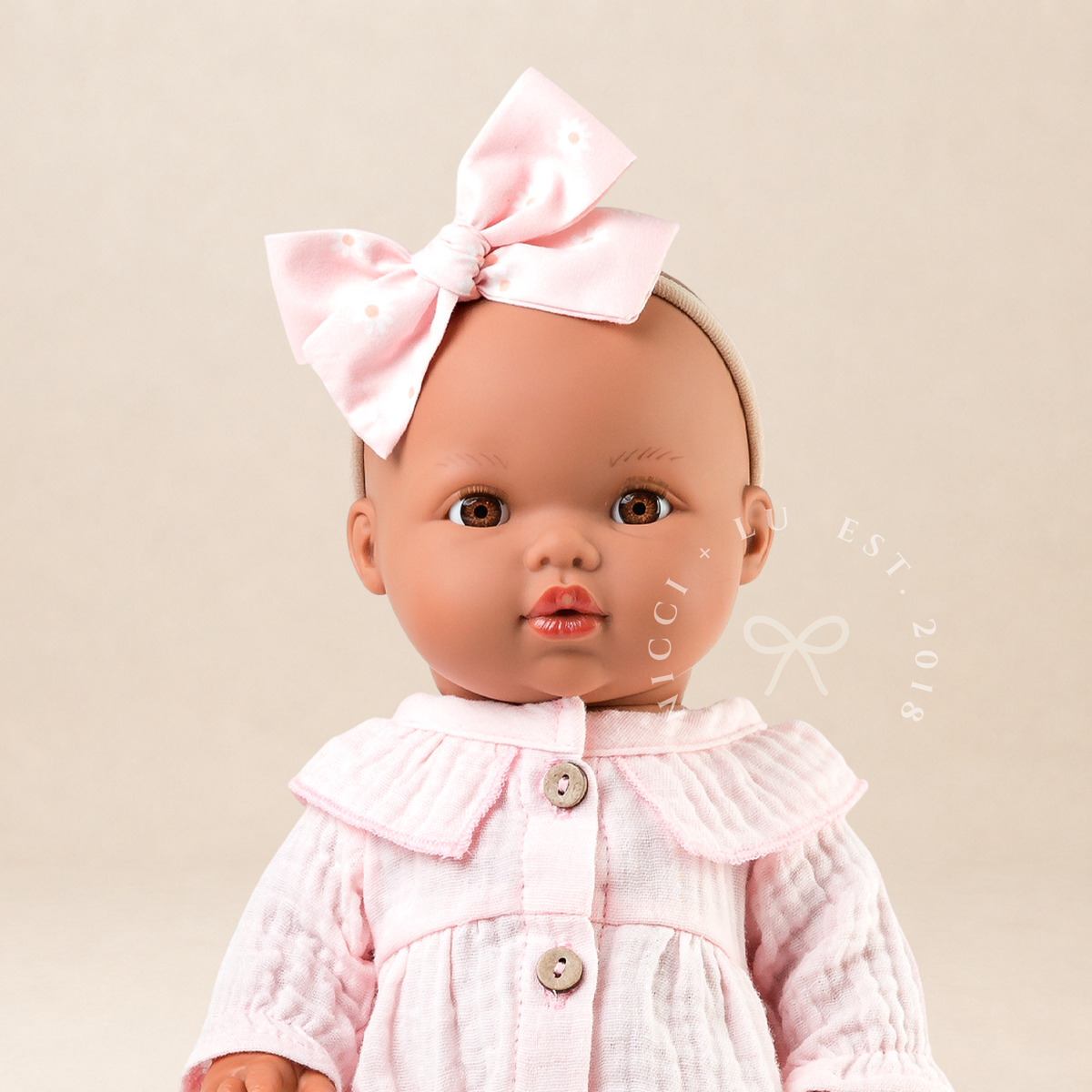 Close-up of 34cm Mini Colettos Alba doll wearing Daisy Muslin Playsuit in Cotton Candy with pink daisy bow by Nicci and Lu.