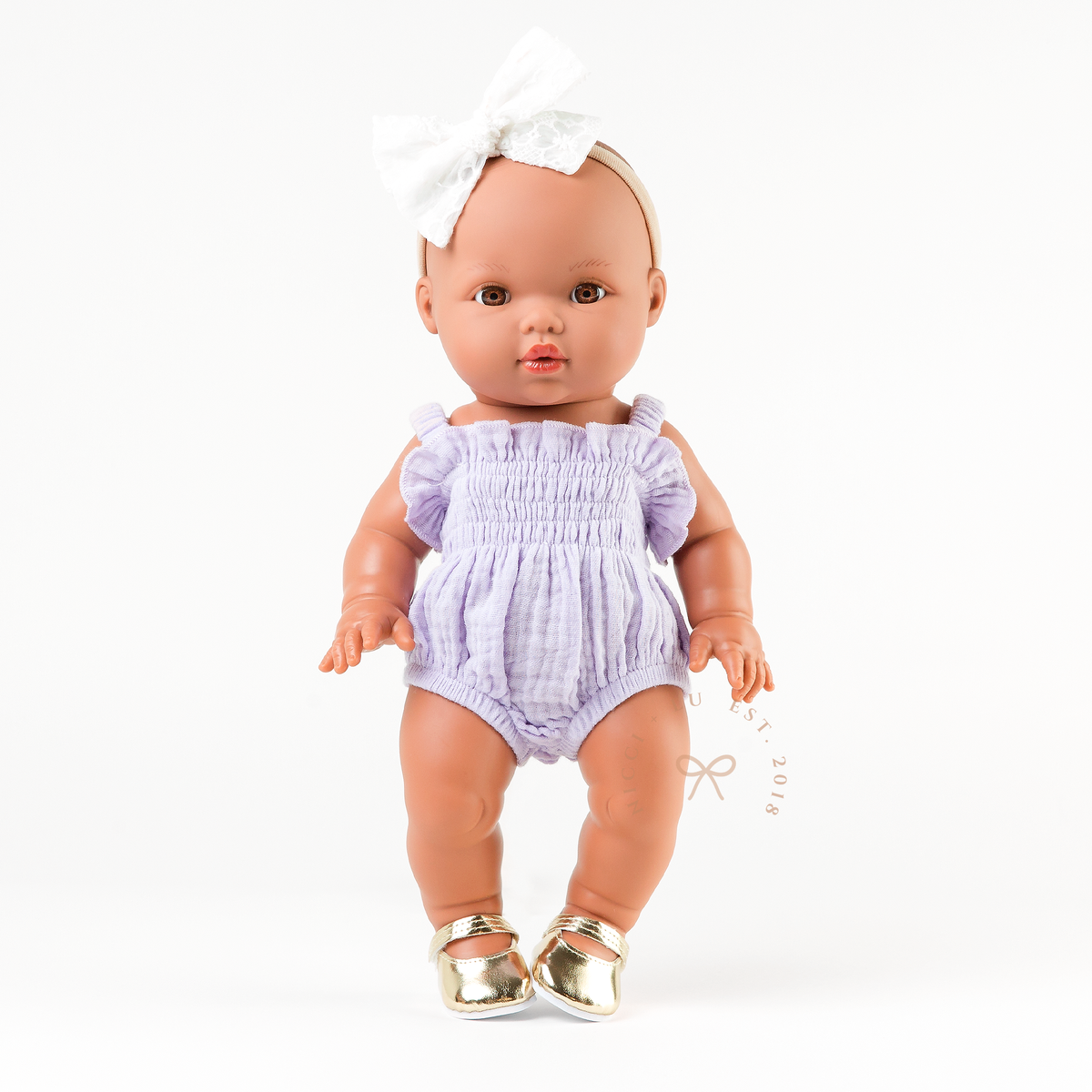 Mini Colettos Alba doll wearing the Olivia Smocked Bubble Romper in Lilac Gingham with gold Mary Jane shoes.