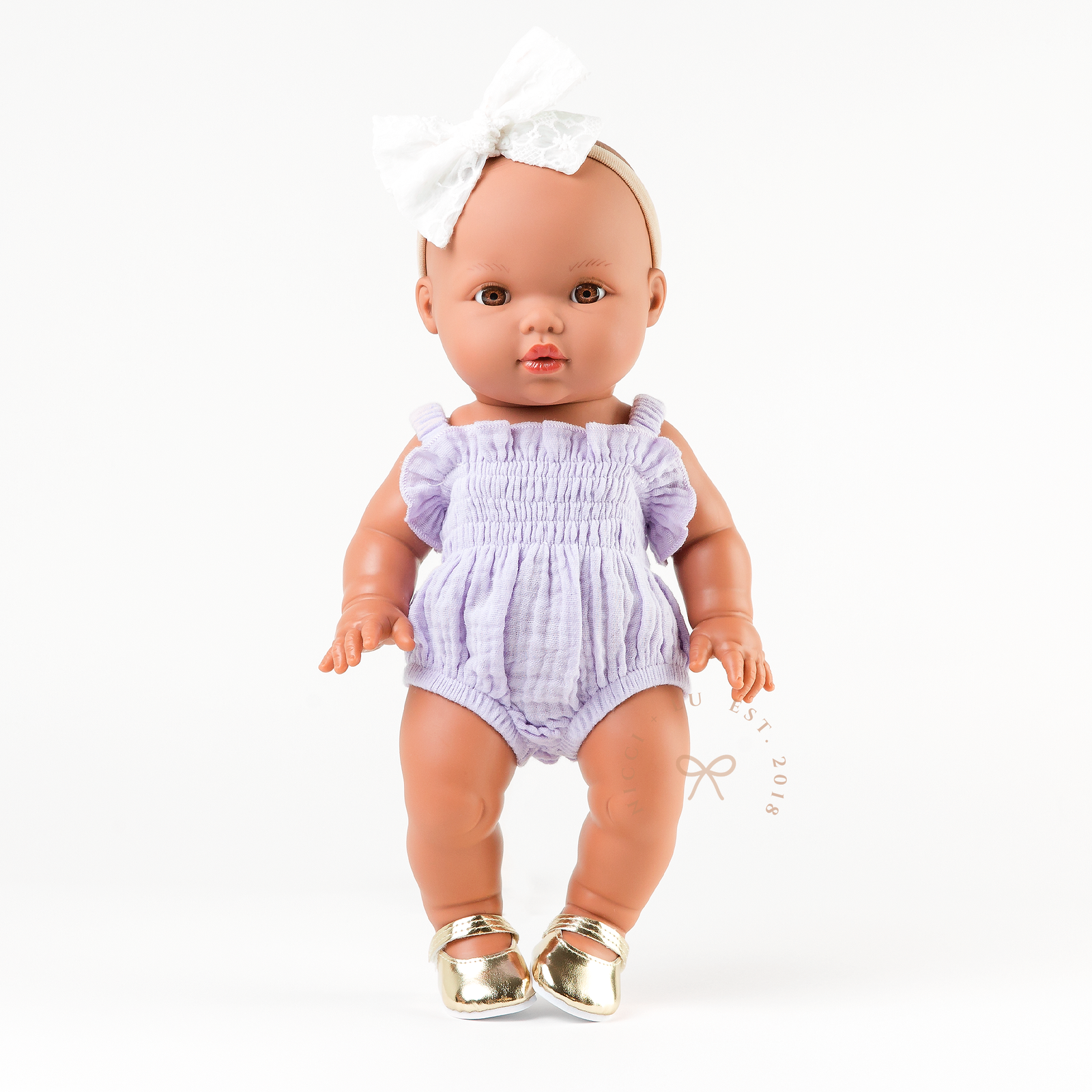 Mini Colettos Alba doll wearing the Olivia Smocked Bubble Romper in Lilac Gingham with gold Mary Jane shoes.