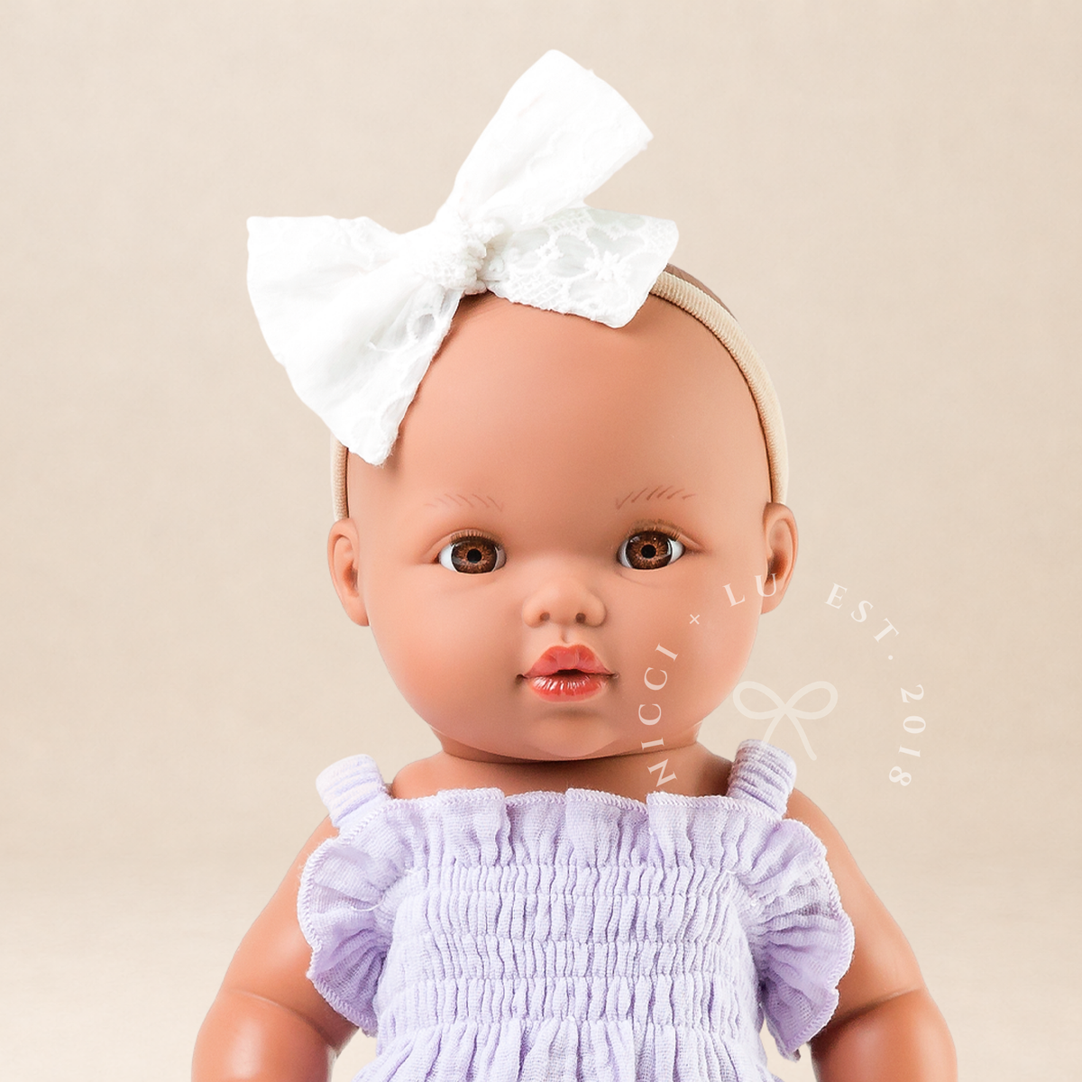 Mini Colettos Alba doll wearing the Olivia Smocked Bubble Romper in Mauve Muslin with a white bow headband.