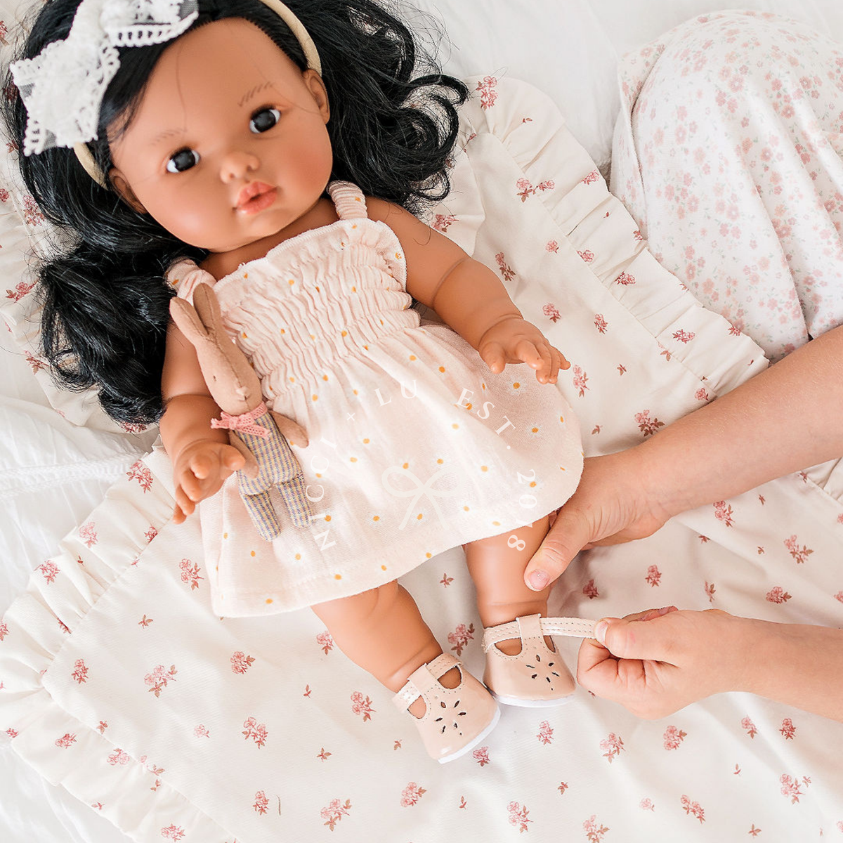 Mini Colettos Aurora wearing the Billie Smocked Dress in Daisy Print Muslin while relaxing on a bed.