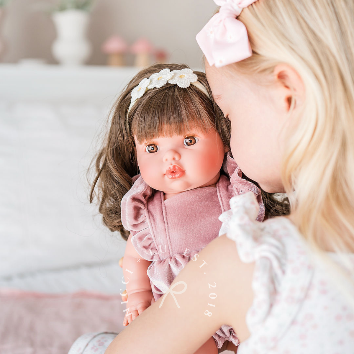 Mini Colettos Hailee wearing the Elodie Frilled Bubble Playsuit in Rose Blush Velvet while being cuddled.