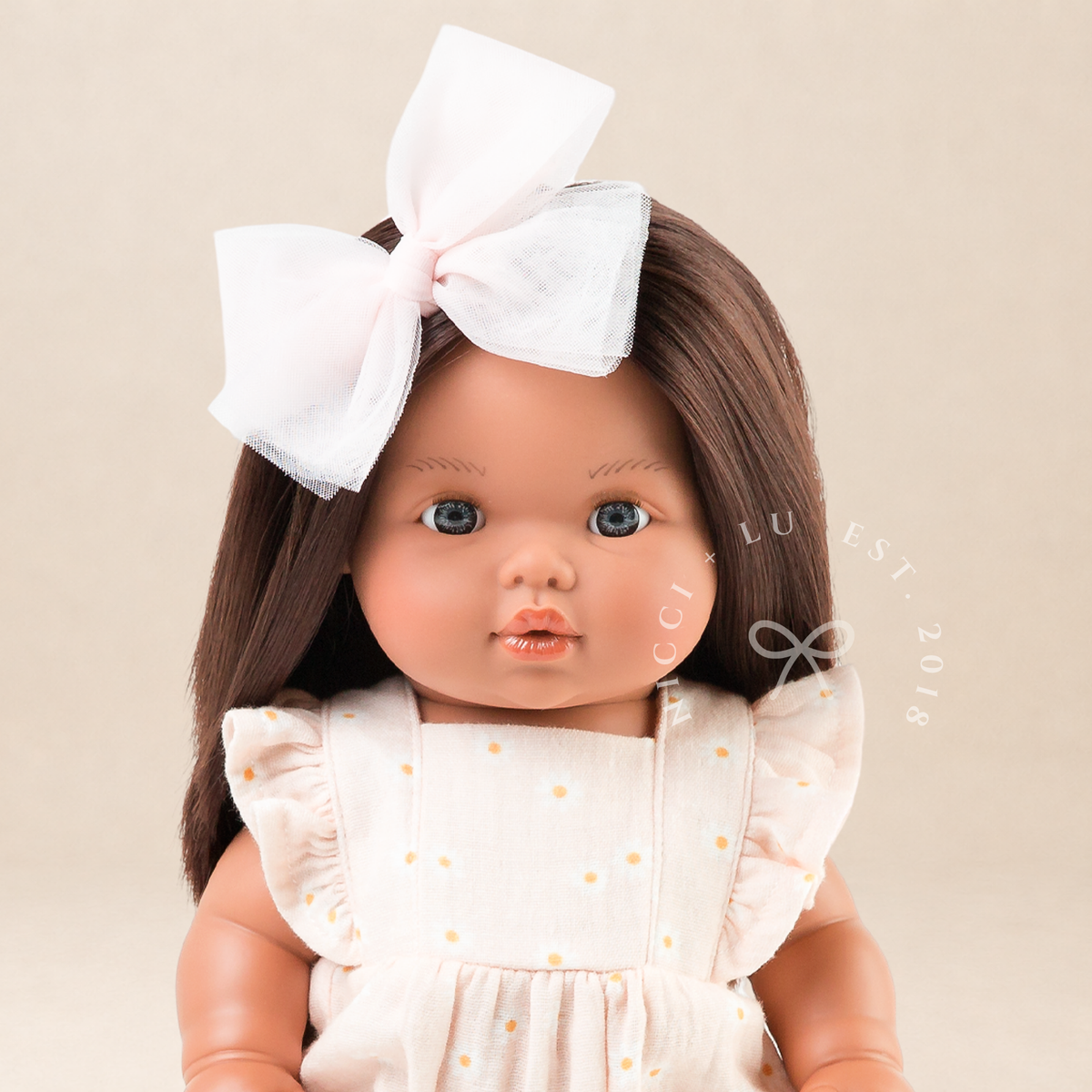 Portrait of Mini Colettos Isabel wearing the Elodie Frilled Bubble Playsuit in Daisy Print Muslin with a pink tulle bow and Gold Mary Jane shoes.