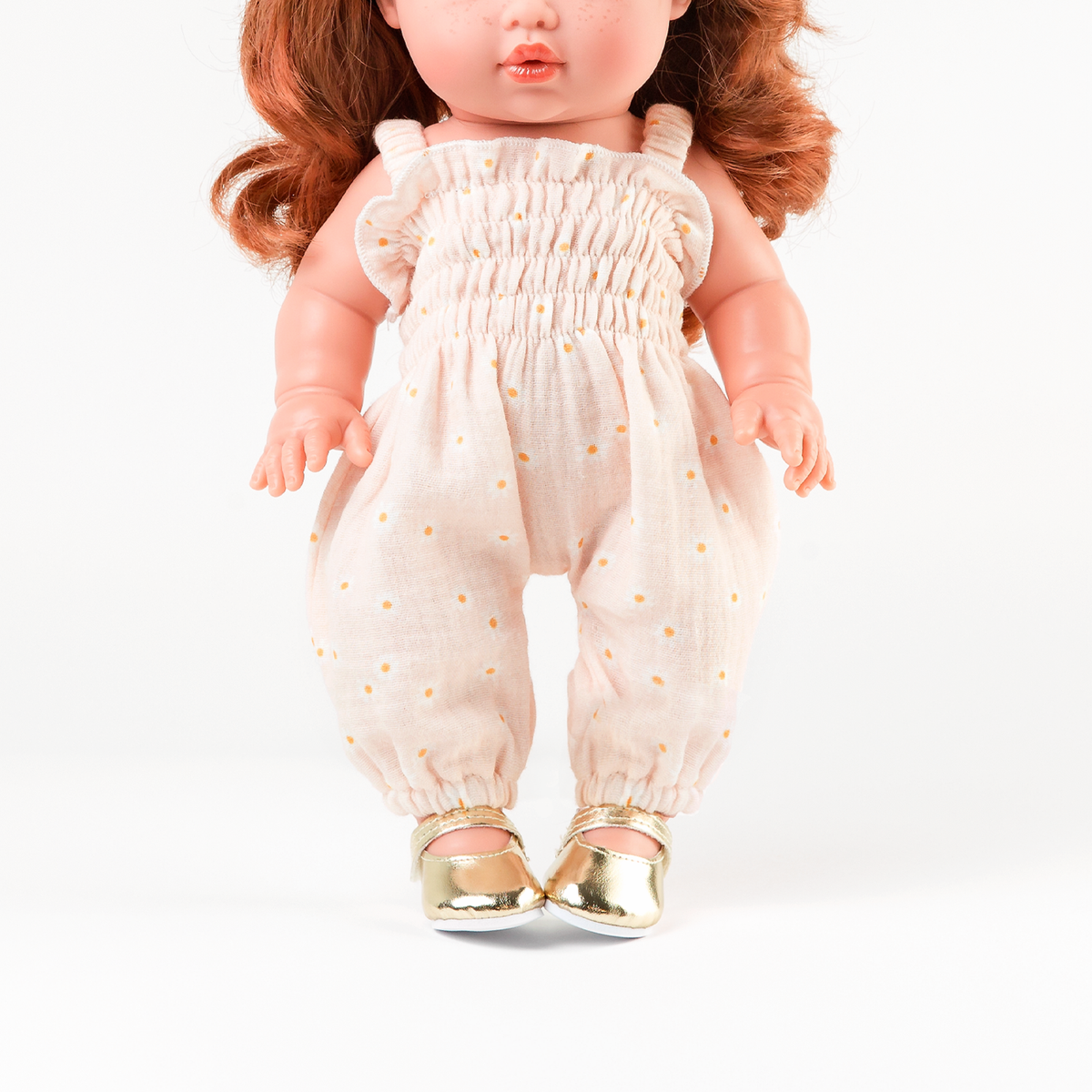 Front view of Mini Colettos Sophia wearing the Florence Smocked Jumpsuit in Daisy Print Muslin with Gold Mary Jane shoes.
