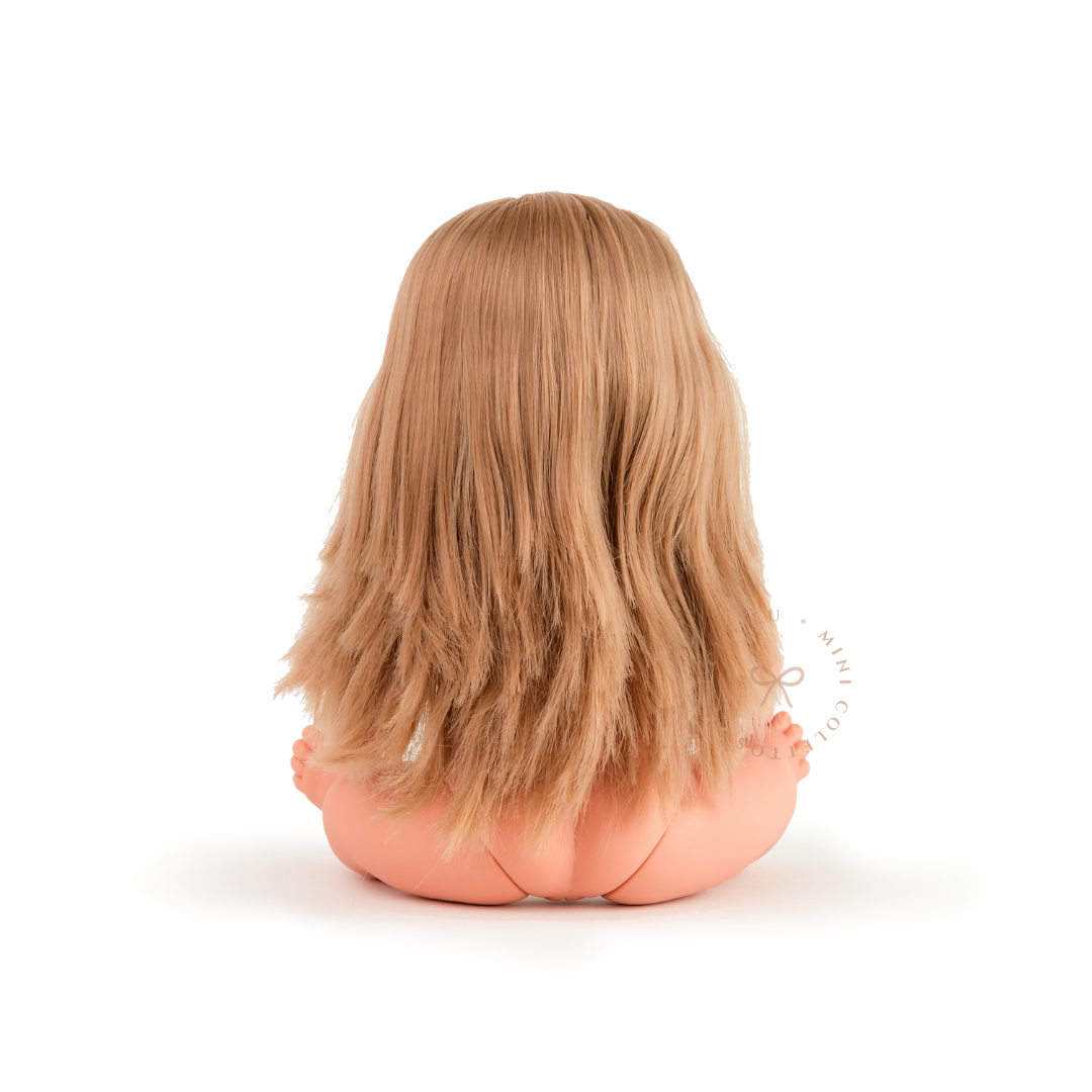Rear view of Mini Colettos Sandra seated undressed, showing her long blonde hair with lightly waved ends.
