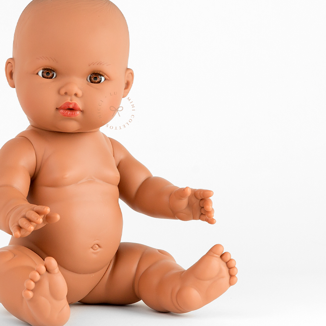 Close-up of Mini Colettos Alba seated undressed, showing her bald head, brown eyes, arms and legs.
