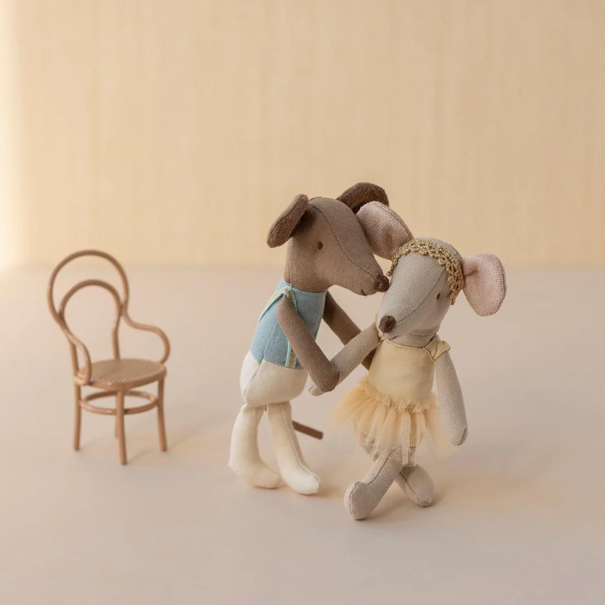 Maileg Ballet Dancer Mouse Big Sister and big brother Two toy mice, one in a blue leotard  and white leggings, the other in a yellow tutu with a gold headband, standing next to a small wooden chair on a beige background.