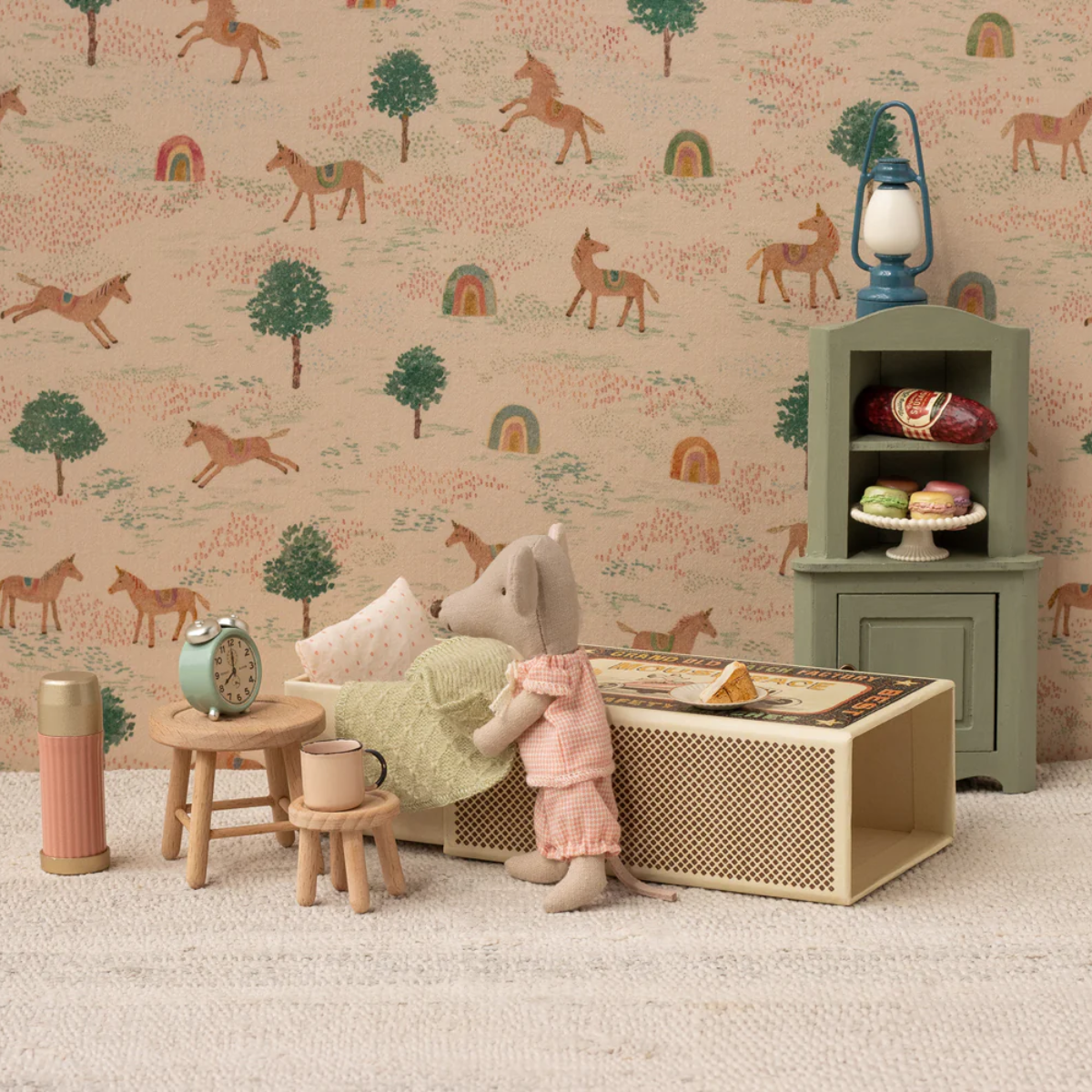 Maileg Little Sister Mouse in Matchbox with toy furniture and decorations against a wallpapered wall.