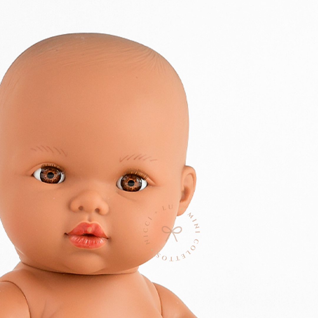 Close-up of Mini Colettos Alba's face, showing her bald head, warm brown eyes and eyelashes.
