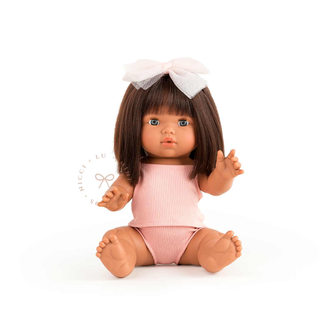 Amaara looks beautiful dressed in a rose blush singlet and undies set with a delicate white hair bow. Her sleek dark-brown bob and sweet expression complete this charming look, showcasing the 34cm Mini Colettos doll styled for imaginative play.