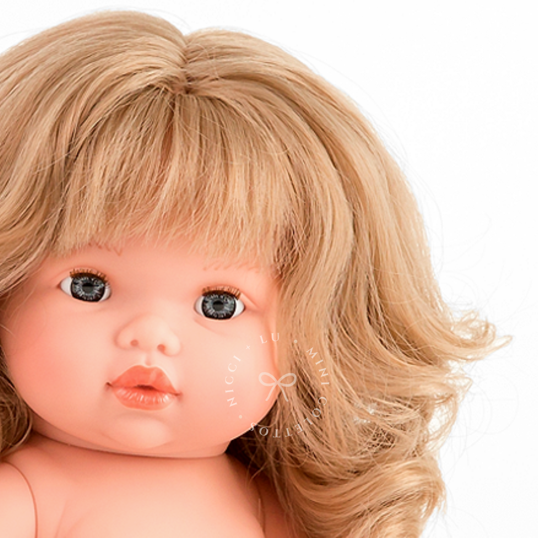 Close-up of Mini Colettos Kate's face, showing blue-grey eyes, a blonde fringe and curls.
