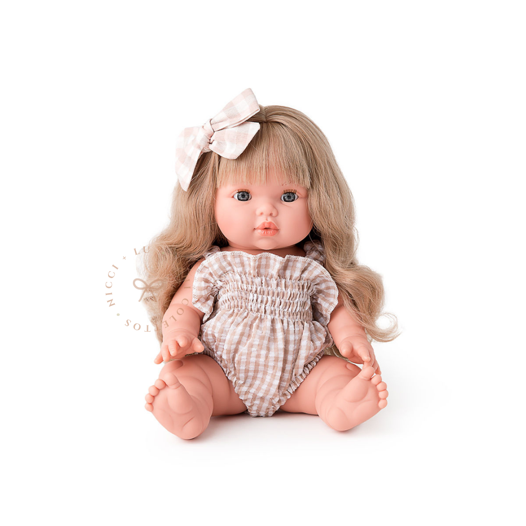 Lyla looks beautiful dressed in a delicate beige gingham olivia smocked bubble romper, finished with a soft white hair bow. Her long blonde curls complement this charming outfit, showcasing the 34cm Mini Colettos doll styled for imaginative play.