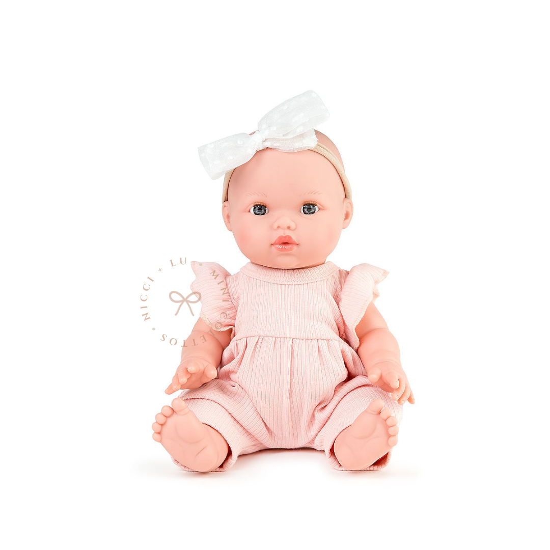 Mila looks adorable dressed in a rose pink lilly ribbed jumpsuit romper with delicate ruffle sleeves and a white bow headband. This styled photograph showcases the 34cm Mini Colettos bald doll dressed for imaginative baby care play.