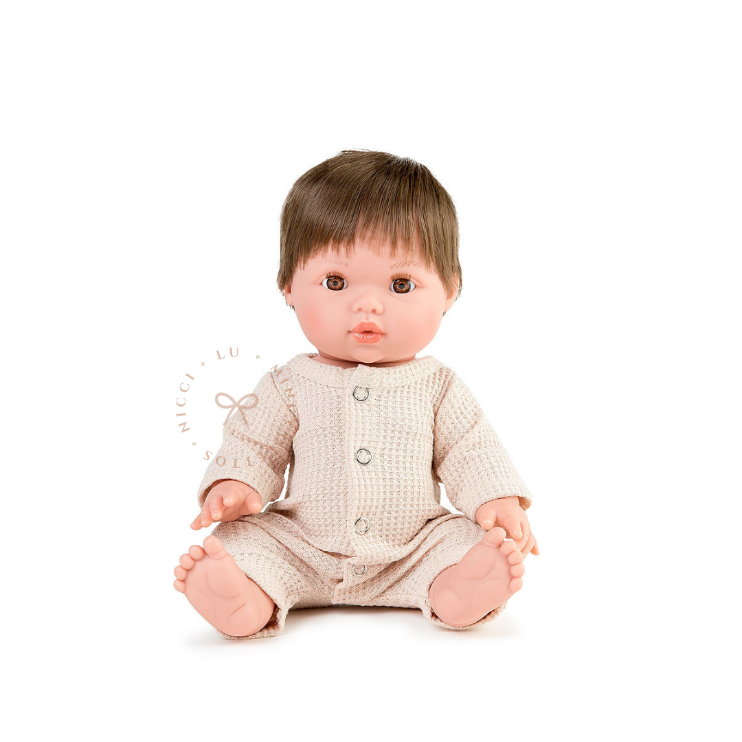 Rafael looks adorable wearing a neutral waffle onesie in oatmeal  with long sleeves and button detailing. This styled photograph showcases the 34cm Mini Colettos doll dressed in a charming outfit for imaginative childhood play.