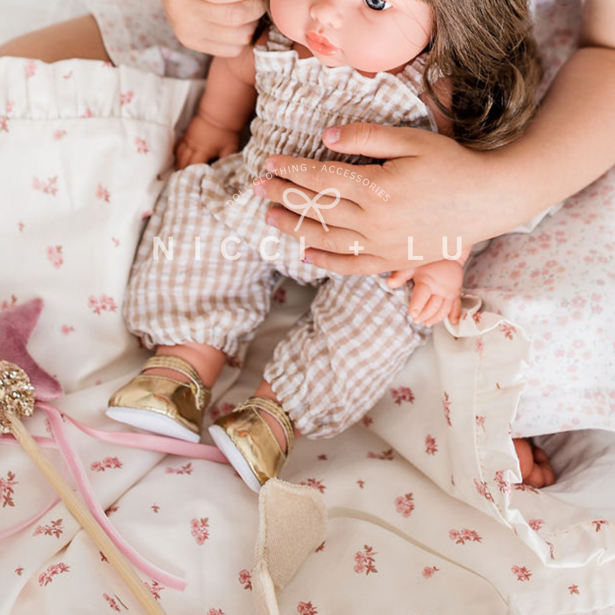 Mini Colettos Hailee is being held by a little girl and she is dressed in a smocked gingham jumpsuit and gold mary jane shoes on a doll comforter set.
