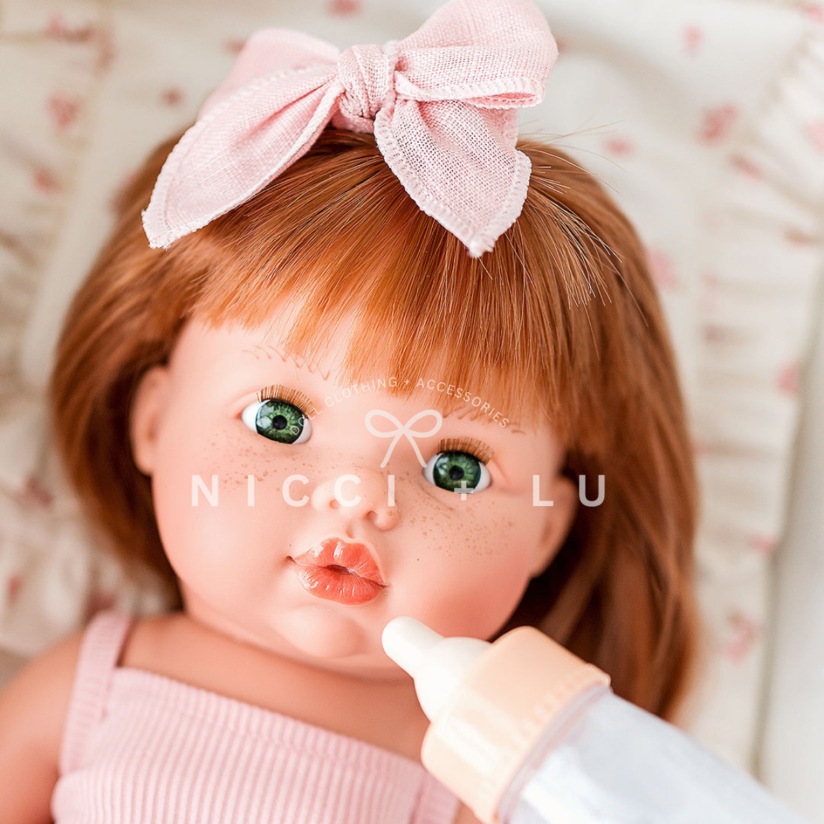 Mini Colettos Nicole is laying down and is being fed a tiny harlow bottle and she is wearing a linen rose blush pink bow.