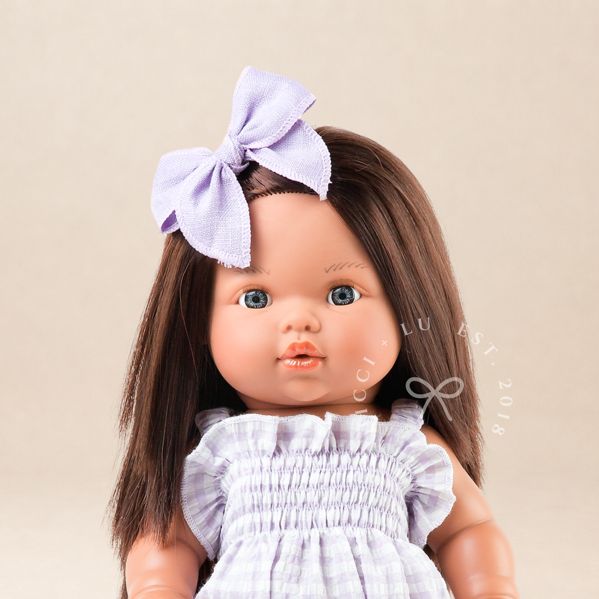 Portrait of Mini Colettos Isabel wearing the Olivia Smocked Bubble Romper in Lilac Gingham with a matching bow.