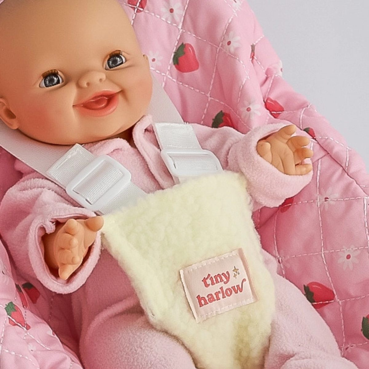Close-up of a doll sitting in the Tiny Harlow Strawberry Picnic car seat capsule