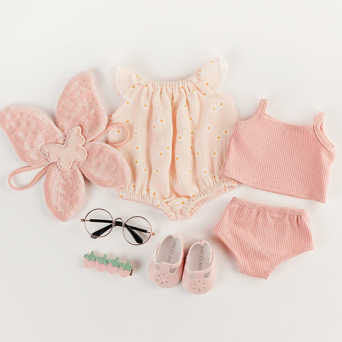 Flat lay featuring the Willow Muslin Romper in Daisy Print, Soft Pink Velvet Fairy Wings, Soft Pink Mary Jane Shoes, Rose Gold Reading Glasses and the Rose Blush Singlet and Undies Set for 34-38cm dolls.